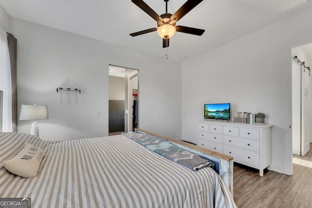 bedroom with a walk in closet, ceiling fan, and wood finished floors