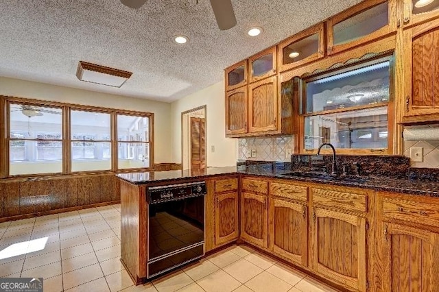 kitchen featuring black dishwasher, dark stone countertops, a sink, and brown cabinets