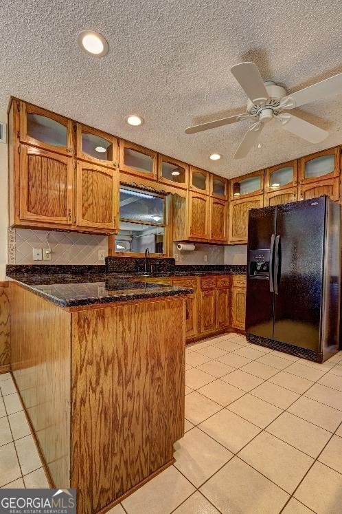 kitchen with a peninsula, dark stone countertops, black fridge with ice dispenser, and brown cabinets