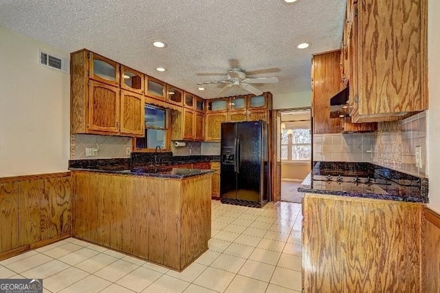 kitchen with visible vents, a wainscoted wall, glass insert cabinets, a peninsula, and black appliances