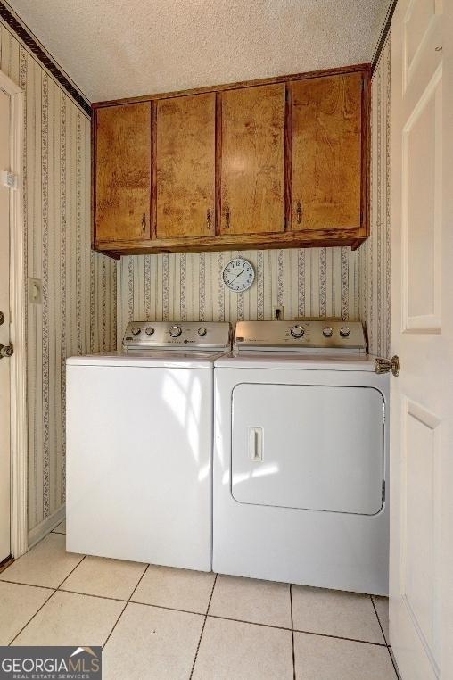 washroom featuring cabinet space, light tile patterned floors, washer and dryer, and wallpapered walls