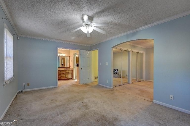 unfurnished bedroom featuring baseboards, arched walkways, ornamental molding, a textured ceiling, and two closets