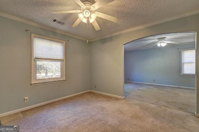 empty room featuring arched walkways, a wealth of natural light, visible vents, light colored carpet, and ornamental molding