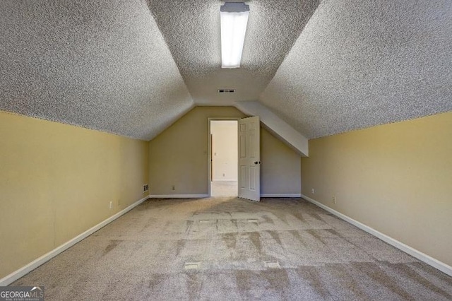 additional living space featuring carpet floors, visible vents, vaulted ceiling, a textured ceiling, and baseboards