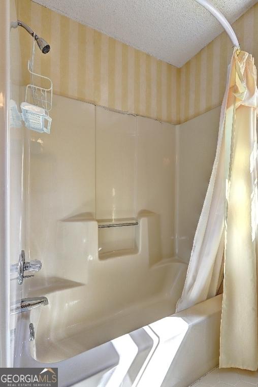 bathroom with shower / bath combination with curtain, a textured ceiling, and wallpapered walls