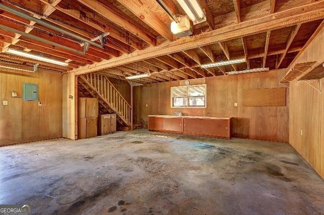 interior space featuring electric panel, wood walls, and unfinished concrete floors