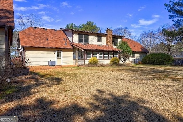 back of property with central AC, a lawn, and a chimney