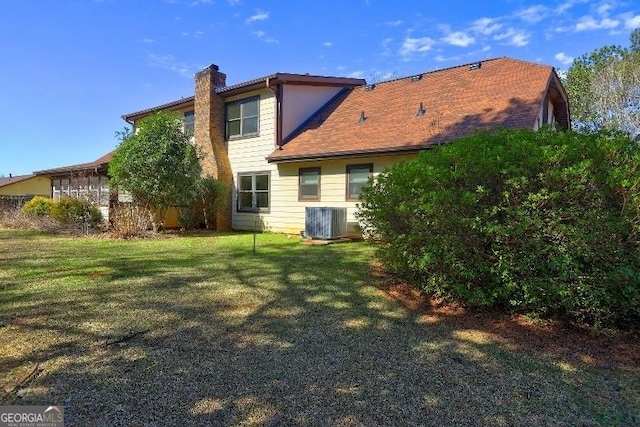 rear view of house featuring a chimney, central AC unit, and a lawn