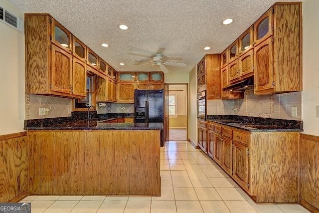 kitchen with visible vents, glass insert cabinets, brown cabinetry, a peninsula, and under cabinet range hood