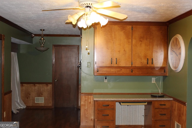 kitchen with a textured ceiling, visible vents, light countertops, wainscoting, and brown cabinetry