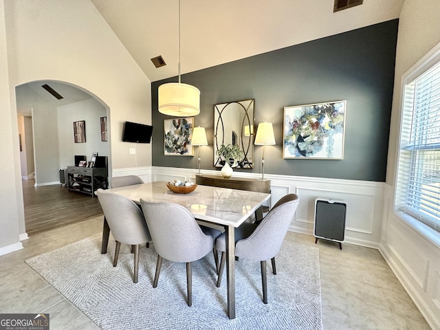 dining room with arched walkways, light tile patterned floors, wainscoting, and lofted ceiling