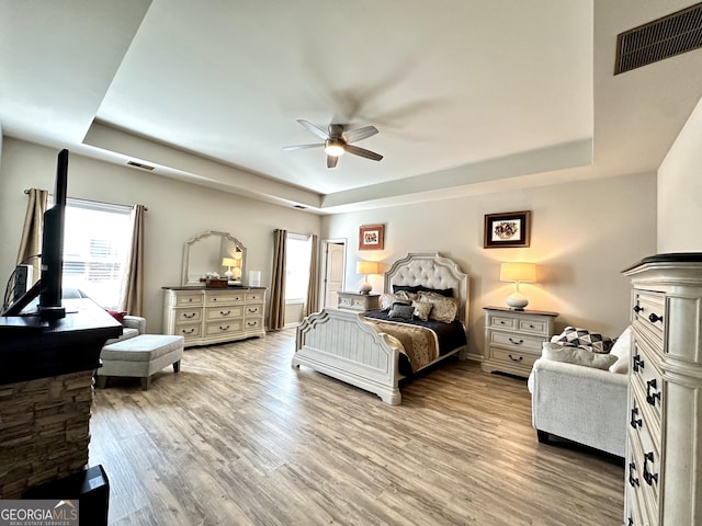 bedroom featuring light wood finished floors, visible vents, and a raised ceiling