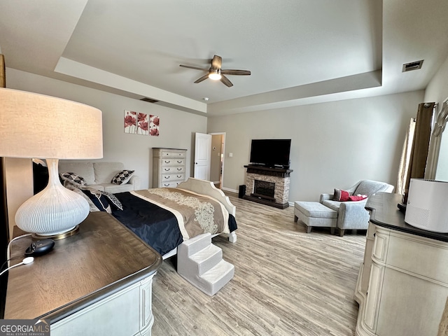 bedroom featuring a tray ceiling, visible vents, a fireplace, and light wood-style flooring