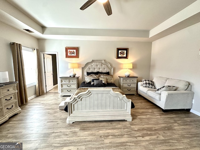 bedroom featuring a tray ceiling, light wood finished floors, visible vents, ceiling fan, and baseboards