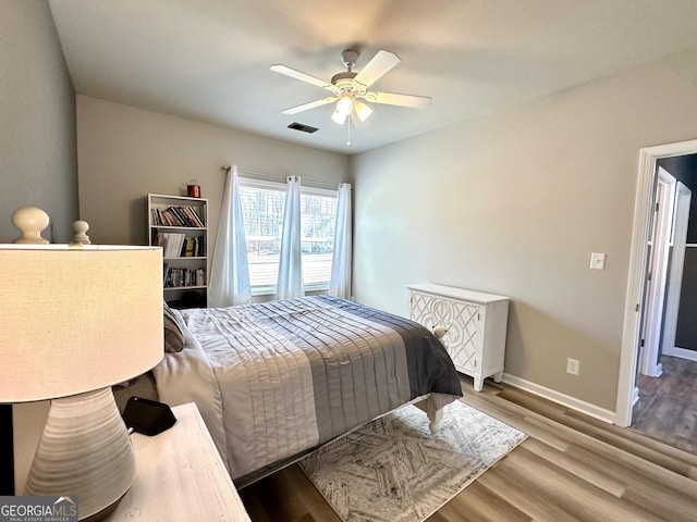 bedroom featuring a ceiling fan, visible vents, baseboards, and wood finished floors