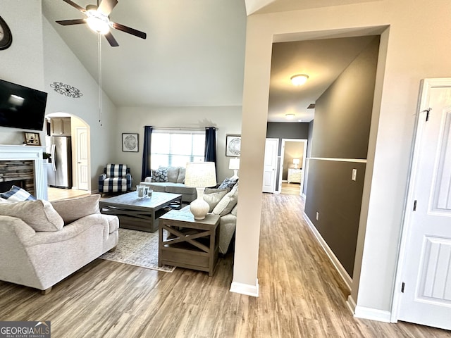 living room with arched walkways, high vaulted ceiling, a fireplace, and wood finished floors