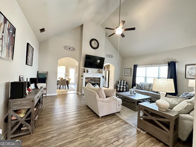 living room with arched walkways, wood finished floors, and a stone fireplace