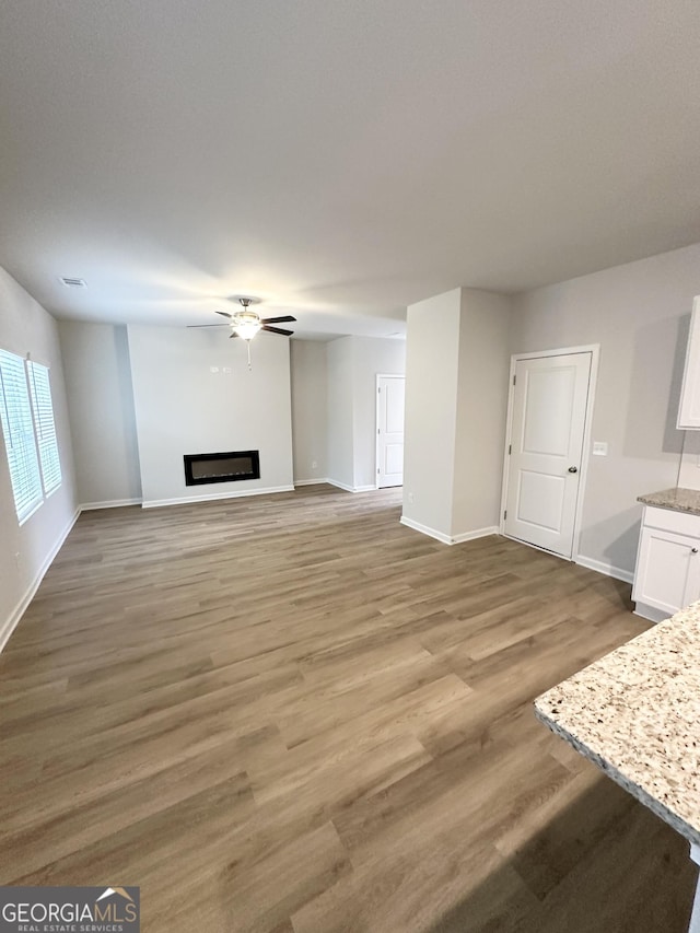 unfurnished living room with ceiling fan, a fireplace, baseboards, and wood finished floors