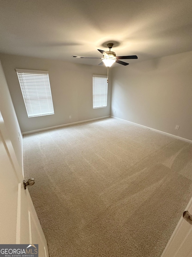 carpeted spare room with a ceiling fan and baseboards