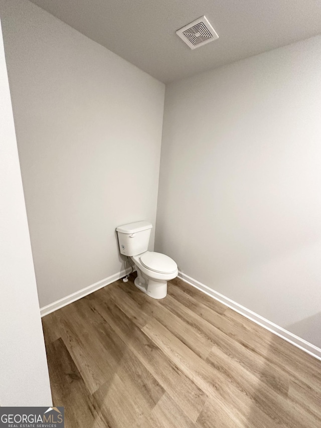 half bath with toilet, wood finished floors, visible vents, and baseboards