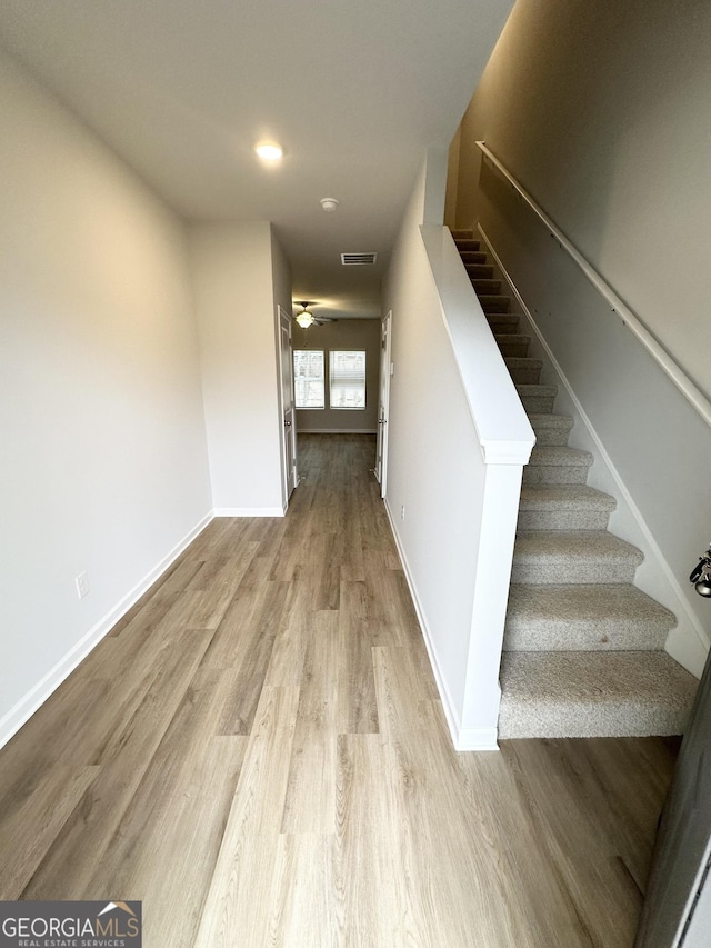 corridor featuring visible vents, light wood-style flooring, baseboards, and stairs