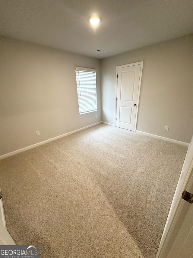 unfurnished room with carpet floors, visible vents, and baseboards