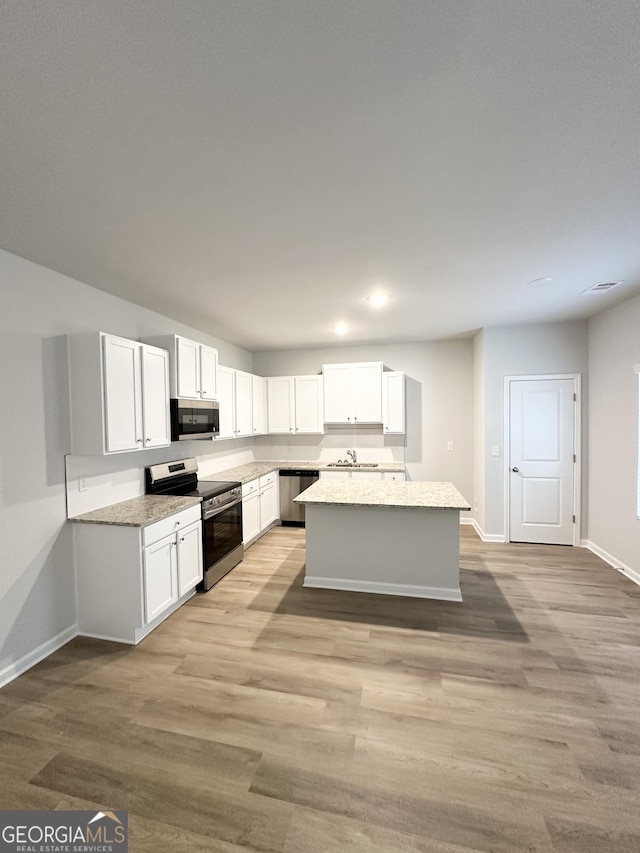 kitchen featuring a center island, appliances with stainless steel finishes, white cabinets, light stone countertops, and light wood-type flooring