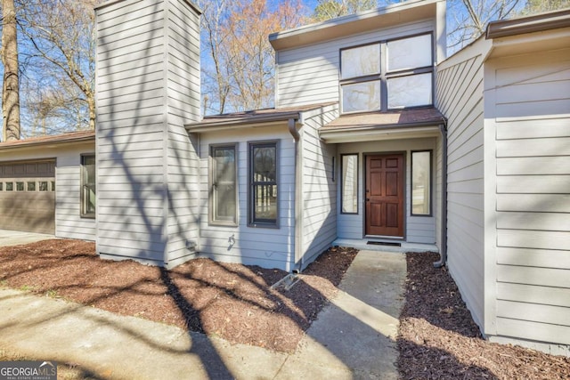 property entrance featuring concrete driveway, a chimney, and an attached garage