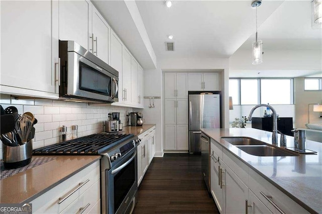 kitchen featuring a sink, white cabinets, hanging light fixtures, appliances with stainless steel finishes, and tasteful backsplash