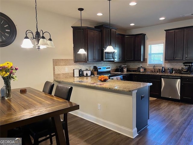 kitchen featuring stainless steel appliances, hanging light fixtures, dark brown cabinets, light stone countertops, and a peninsula