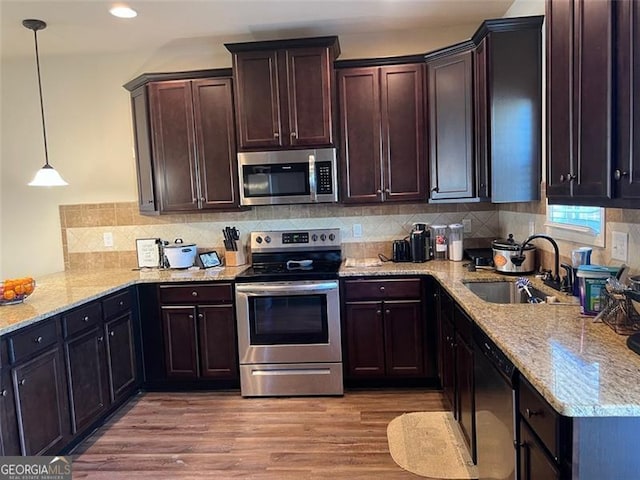 kitchen with light wood-style flooring, decorative light fixtures, stainless steel appliances, dark brown cabinets, and a sink