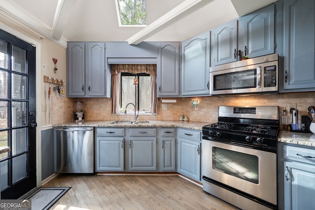 kitchen featuring light stone counters, stainless steel appliances, a sink, backsplash, and beamed ceiling