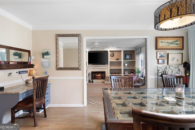 dining room featuring light wood-style floors, a lit fireplace, baseboards, and ceiling fan