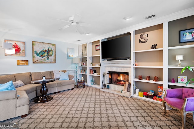 carpeted living room featuring ceiling fan, built in shelves, visible vents, a brick fireplace, and crown molding
