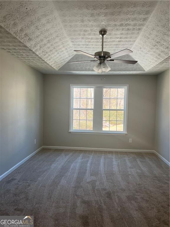 spare room featuring carpet, a ceiling fan, vaulted ceiling, a textured ceiling, and baseboards