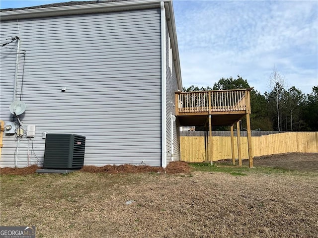 view of side of property with central AC, fence, a wooden deck, and a lawn