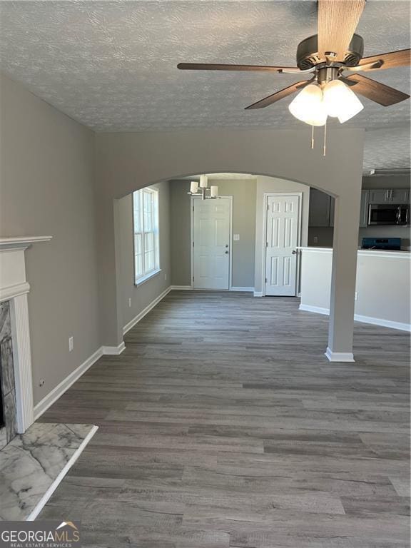 unfurnished living room featuring arched walkways, a textured ceiling, a fireplace, and wood finished floors