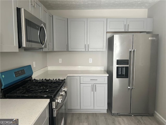 kitchen featuring light wood-style flooring, light stone counters, stainless steel appliances, a textured ceiling, and gray cabinetry