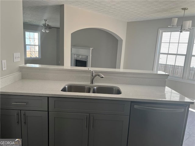 kitchen featuring gray cabinetry, a sink, dishwashing machine, and light stone countertops