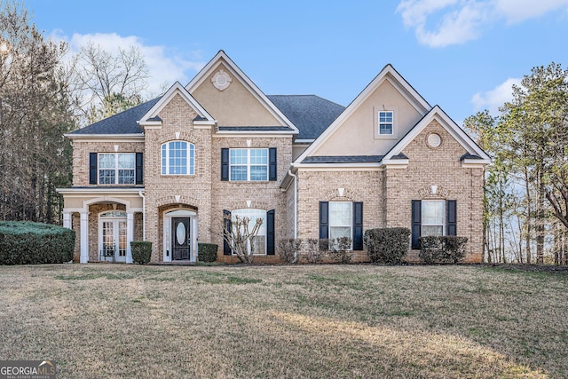 traditional home with french doors, brick siding, stucco siding, a shingled roof, and a front lawn