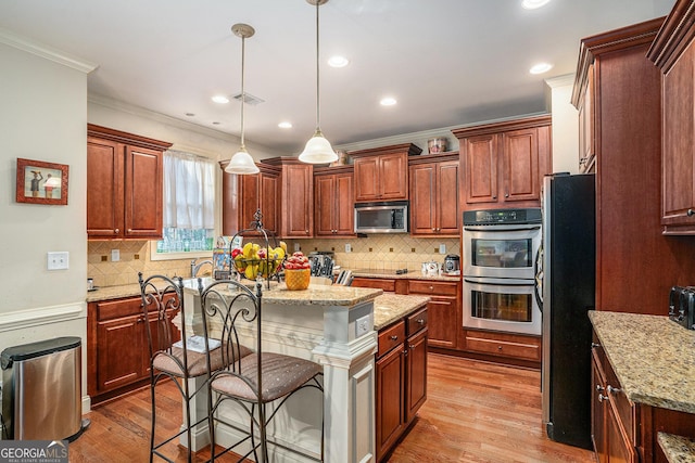 kitchen featuring a breakfast bar, a center island, light wood-style flooring, appliances with stainless steel finishes, and light stone countertops