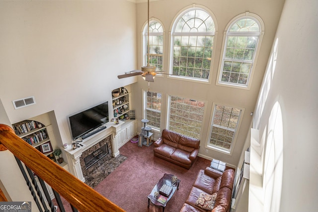 living area featuring a high ceiling, a fireplace with flush hearth, carpet flooring, visible vents, and a ceiling fan