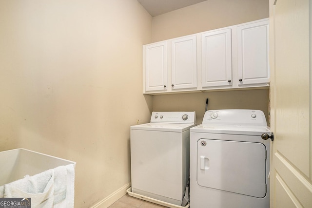 laundry area featuring light tile patterned flooring, washing machine and dryer, cabinet space, and baseboards