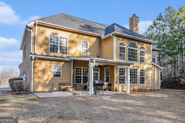 back of house featuring a shingled roof, a chimney, and a patio