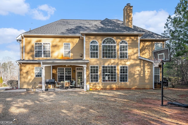 back of house with a shingled roof, a chimney, a ceiling fan, and a patio