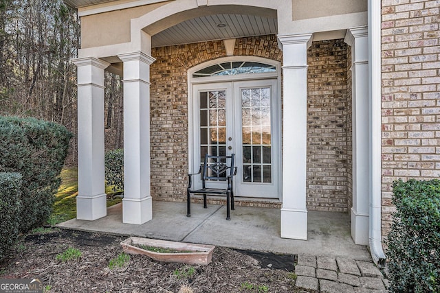 view of exterior entry featuring covered porch, french doors, and brick siding