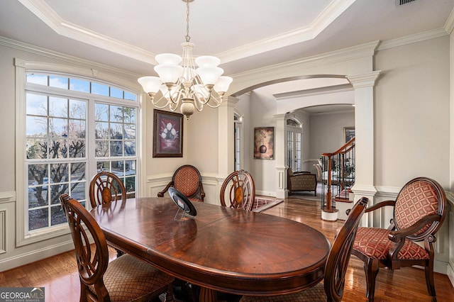 dining space with a tray ceiling, crown molding, arched walkways, and wood finished floors