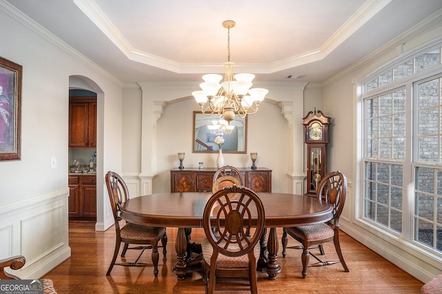 dining room with a tray ceiling, an inviting chandelier, ornate columns, and wood finished floors