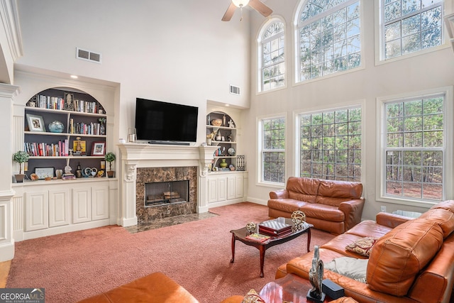 carpeted living area featuring ceiling fan, built in shelves, a premium fireplace, and visible vents