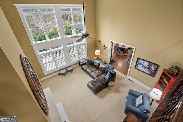 living area with carpet, baseboards, ceiling fan, and a high ceiling